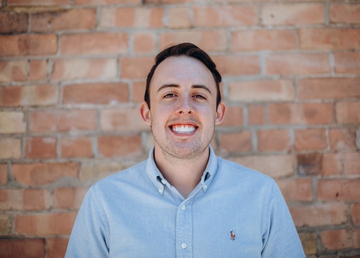 tyler mcginnis creator of advanced javascript stands in front of brick wall wearing a blue polo shirt